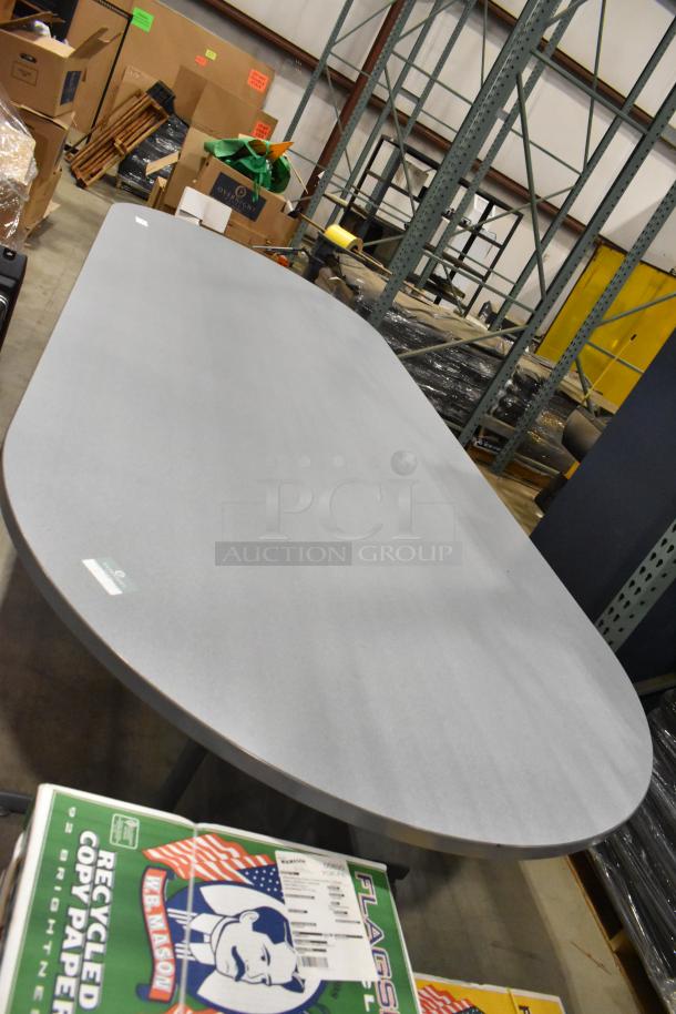 Gray oval table in a warehouse setting, smooth tabletop, sturdy condition, suitable for office or dining use.