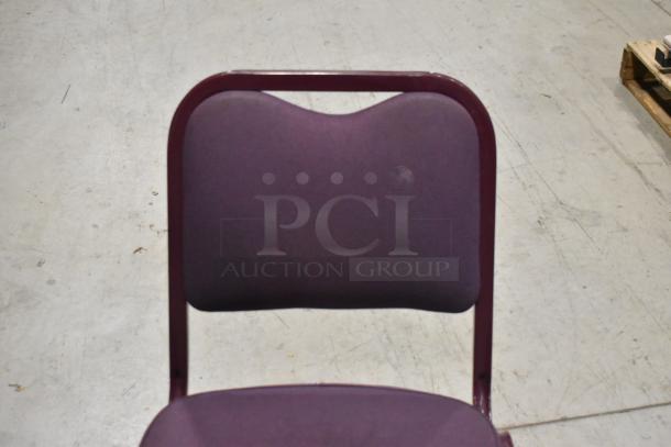 Maroon metal chair with maroon seat and backrest, shown in warehouse, sturdy design, in good condition. Auction includes 20 chairs.
