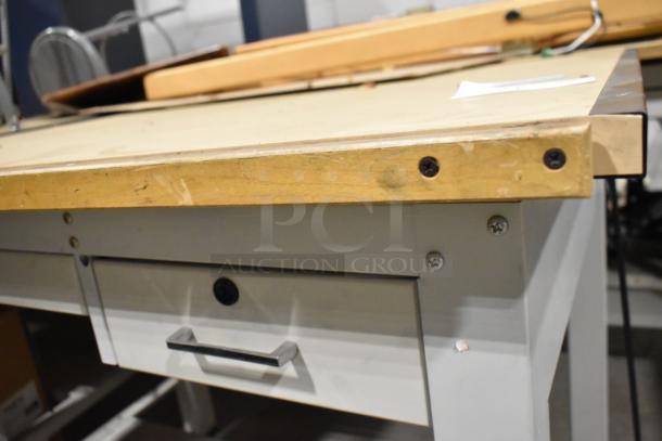 Gray metal table with a wooden tabletop, features a drawer and visible screws. Moderate condition, suitable for workshop use.