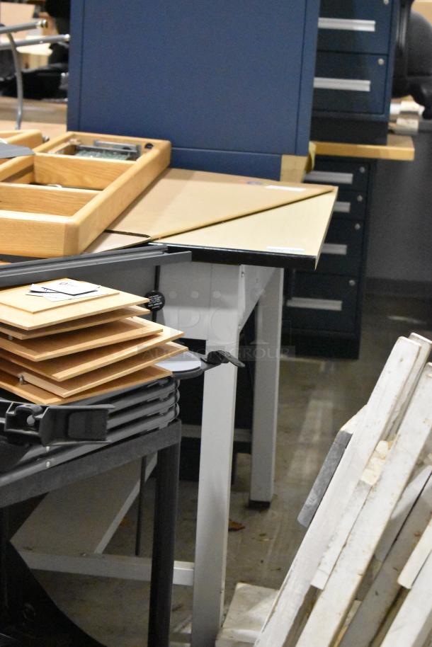 Three gray metal tables with wooden tabletops, stacked wood panels nearby, in a workshop setting. Good condition.
