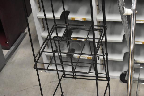 Metal newspaper stand and laundry bag frame on casters, auction item, visible shelving unit in the background.