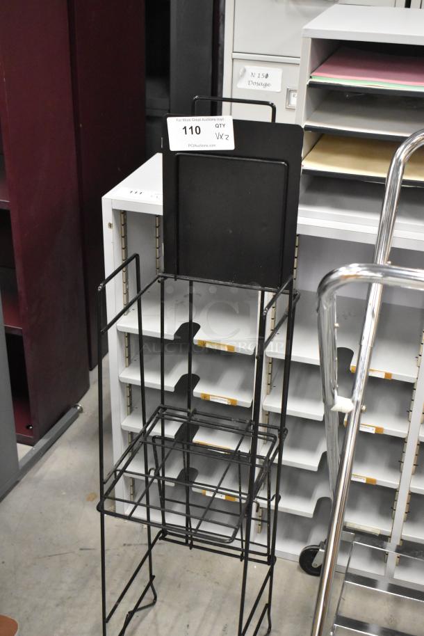 Metal laundry bag frame on casters and a black newspaper stand, quantity two per bid. Good condition.