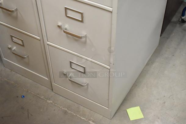 Two gray metal four-drawer filing cabinets in good condition, featuring label slots and sturdy handles.