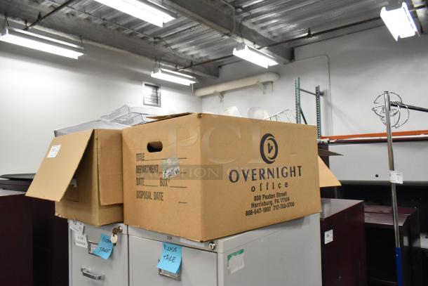 Cardboard boxes labeled "Overnight Office" containing various items like staplers, racks, and bins, showing signs of warehousing.