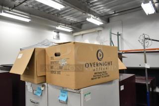 Cardboard boxes labeled "Overnight Office" containing various items like staplers, racks, and bins, showing signs of warehousing.