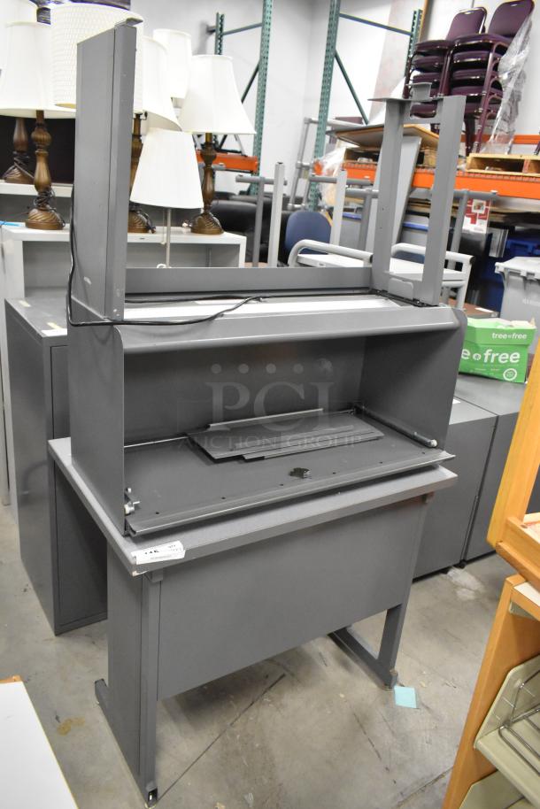 Gray desk with overhead cabinet, metal construction, moderate wear, includes partial assembly components and cable.