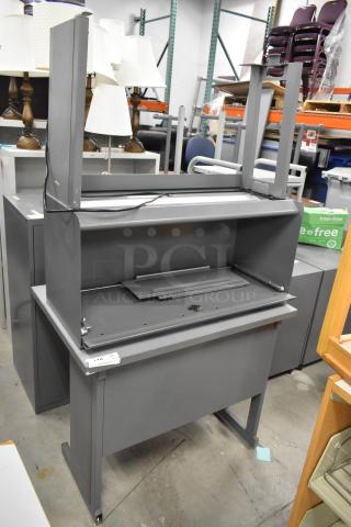 Gray desk with overhead cabinet, metal construction, moderate wear, includes partial assembly components and cable.
