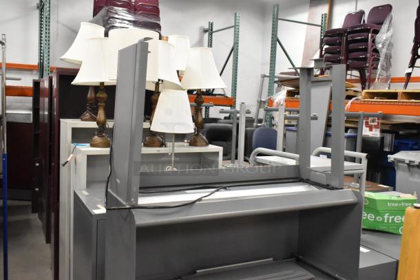 Gray desk with overhead cabinet, disassembled, in storage. Features sturdy metal frame. Condition appears used.