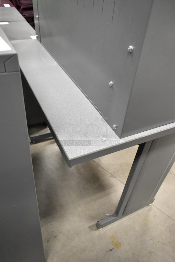 Gray desk with overhead cabinet, featuring metal construction and sturdy legs. Minor wear visible on the surface.