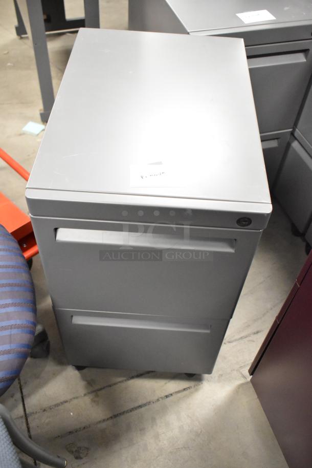 Gray 2-drawer filing cabinet on casters, shown with label. Features metal construction, minor surface wear.