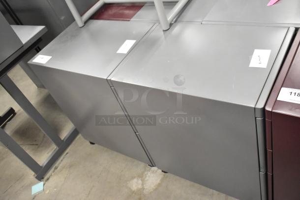 Four filing cabinets on casters; includes two gray two-drawer, and one maroon three-drawer. Good condition. Auction labels visible.