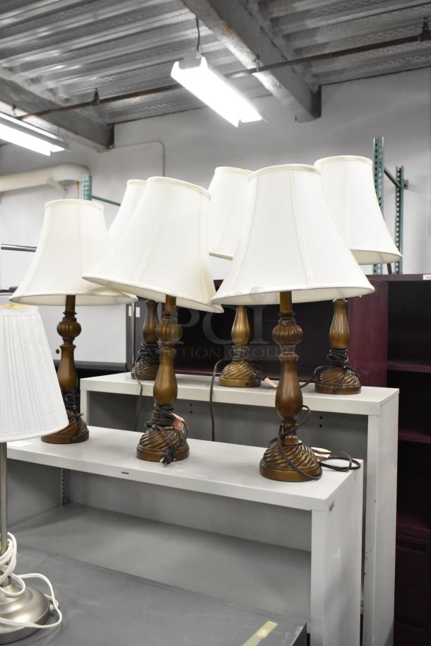 Eight assorted table lamps with white shades on display, featuring wooden and metal bases. Good condition.