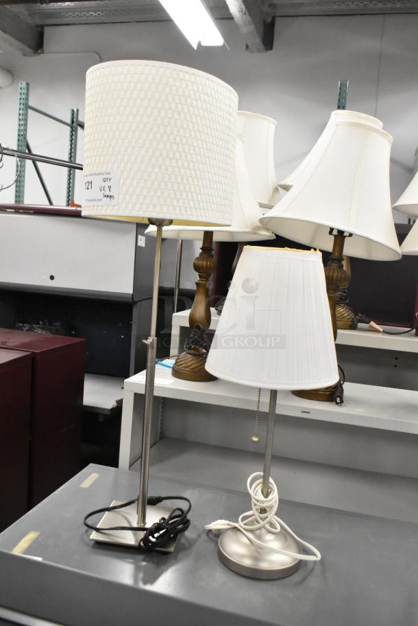 Eight assorted lamps with varying designs, white shades, metal bases, and visible cords, in good condition with auction tags.