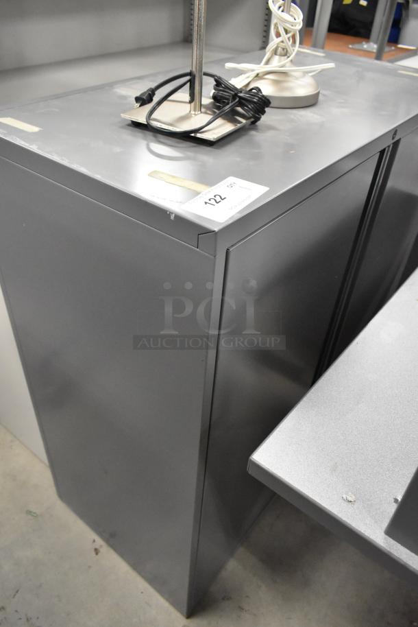 Gray metal 2-door cabinet in good condition. Features a sleek design. Auction label "Lot 122" visible on top.