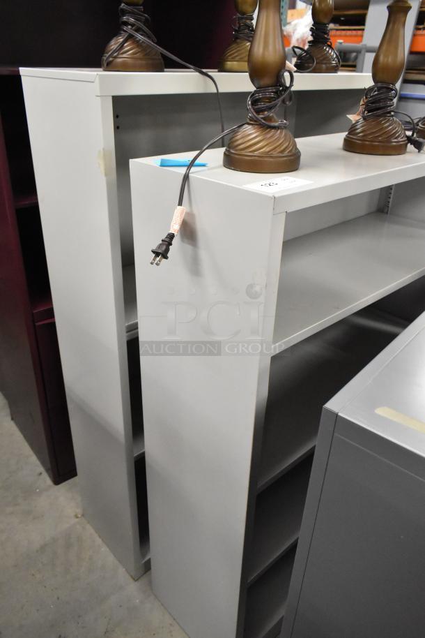 Two gray bookshelves, used condition, featuring multiple shelves for storage. Auction offers bid multiplier.