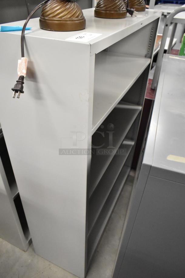 Two gray bookshelves, metal, four adjustable shelves each, good condition, minor scratches, ideal for office use.