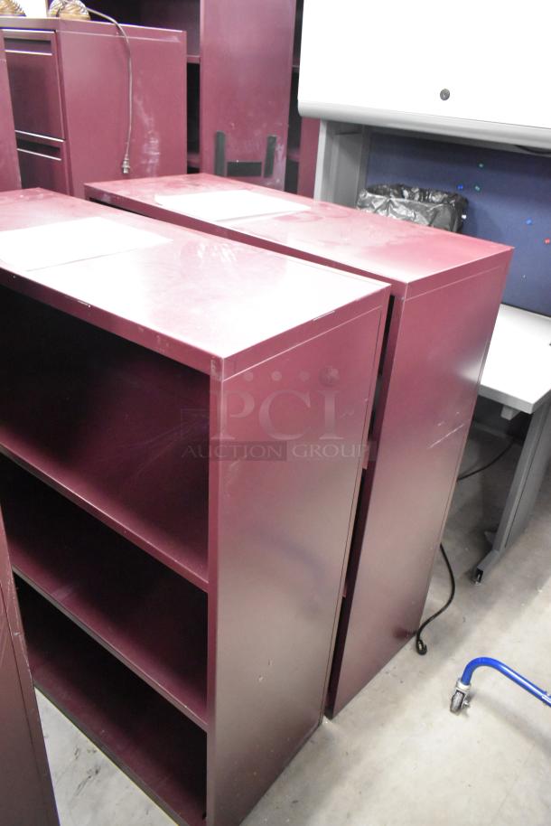 Two maroon metal bookshelves, each with three shelves. Slight surface wear visible. Ideal for storage or organization.