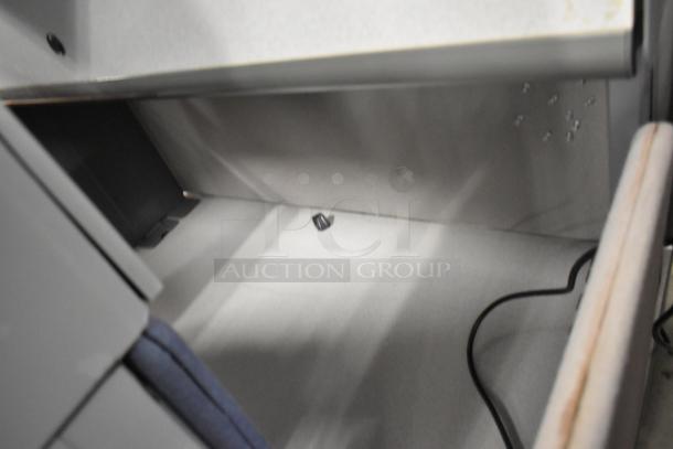 Light gray desk area with overhead cabinet, showing a clean surface and a small electronic component. Desks sold in pairs.