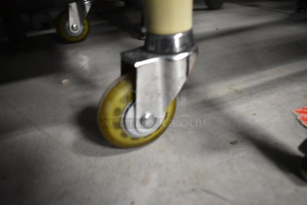 Close-up of a caster wheel on a 3-tier cart. Yellow wheel with metal bracket, in good condition, on concrete floor.