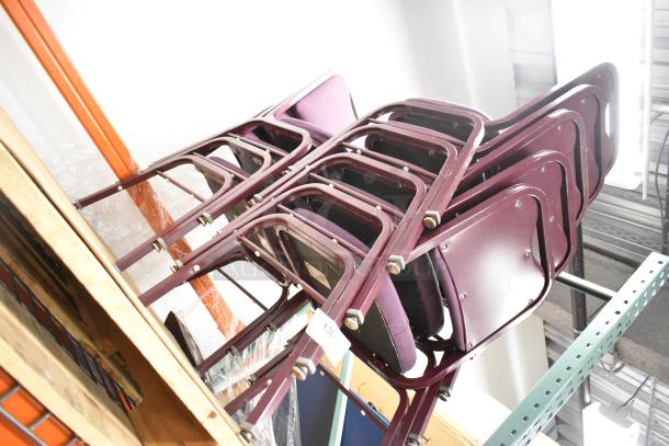 36 maroon metal chairs with maroon cushions and backrests, stacked in storage. Appears in good condition.