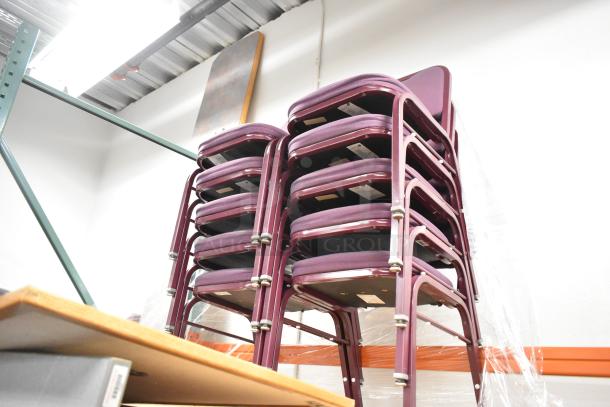 36 maroon metal chairs with maroon cushions and backrests, stacked in a warehouse. Good condition, auction item lot.