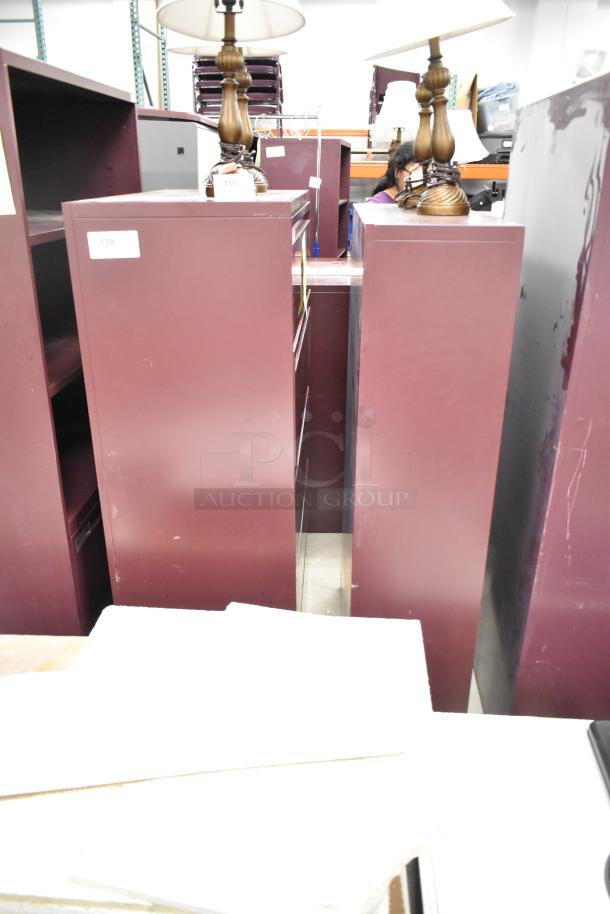 Two metal maroon bookshelves, tall and narrow, showing minimal wear. Suitable for office or home use. Auction item.