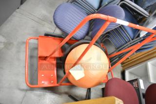 Orange metal cart on casters holding an exercise ball, sturdy frame, optimal for transporting items. Appears in good condition.