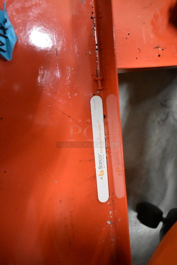 Orange metal cart on casters, shows wear with scratches and marks. Barco "Love What You Wear" label visible.