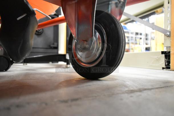 Orange metal cart on casters, highlighting a sturdy wheel and metal frame, ideal for storage or transport needs.