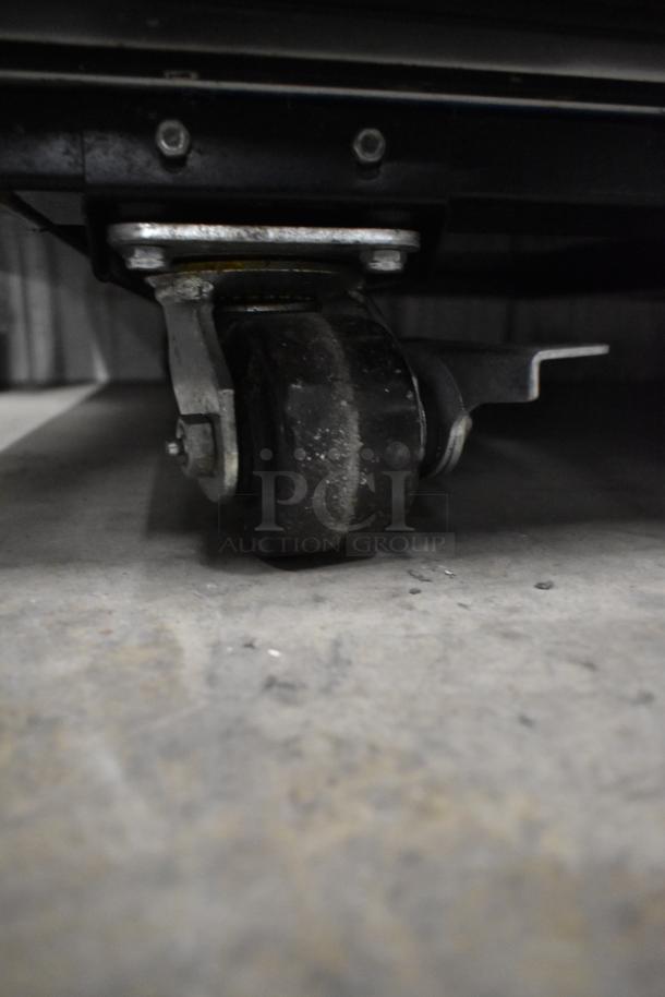 Close-up of the commercial caster of a 2022 True TG2R-2S-HC stainless steel cooler, showcasing wear on the wheel.