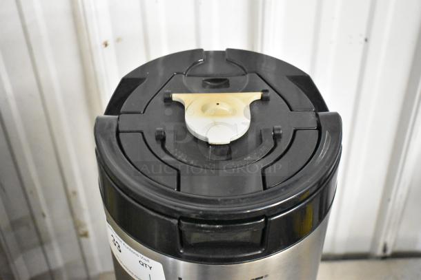 Fetco L4S-15 Luxus beverage holder dispenser, stainless steel, black lid, visible label, good condition.