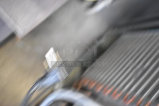 Blurry image of a Delfield 406P-STAR2 stainless steel undercounter cooler, on casters, showing part of an electrical cord.