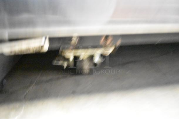 Blurry image showing the base and caster wheel of a commercial cooler, possibly the True TG2R-2S-HC model.