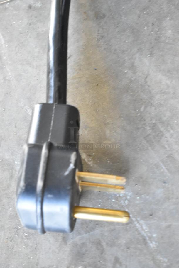 Close-up of a power plug for a Cooking Performance Group Model 351ICRCPG2M induction range. Black with two brass prongs.