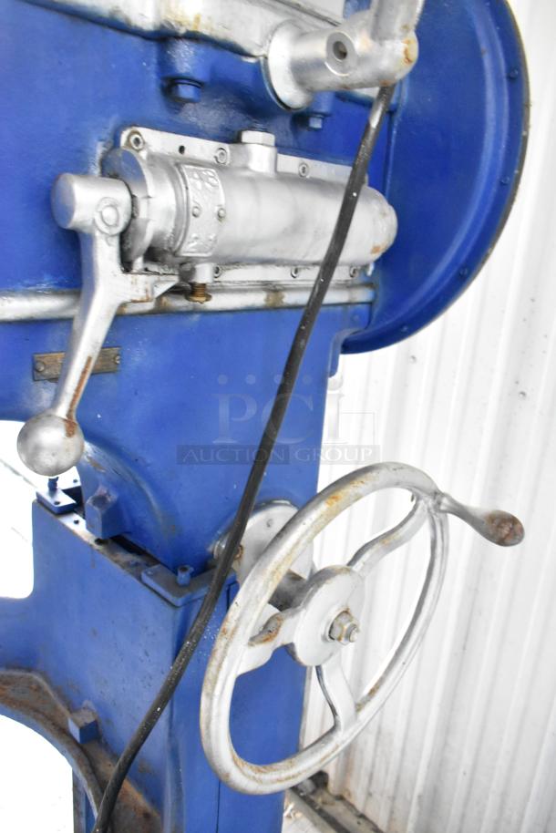 Metal commercial floor style planetary dough mixer, blue and silver, with manual control levers. Visible wear on handle.