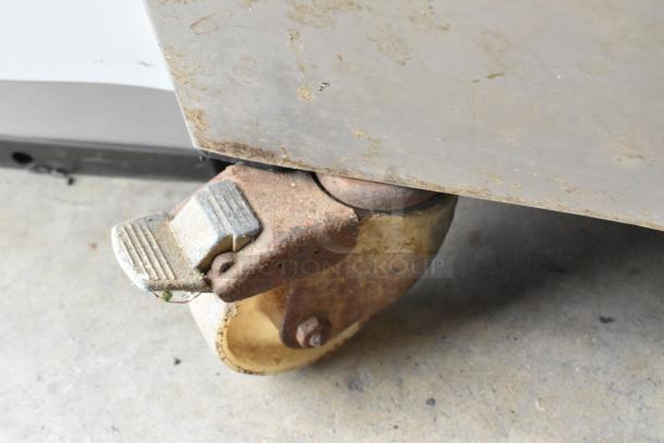 Bizerba stainless steel commercial vacuum sealer on caster wheels. Visible caster shows wear and rust, indicating use.