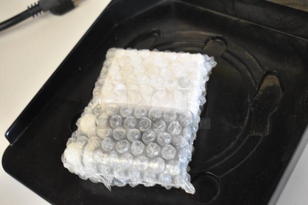 Bubble-wrapped item on black tray; unclear details, potential part for Newco ACE-TS Coffee Machine.