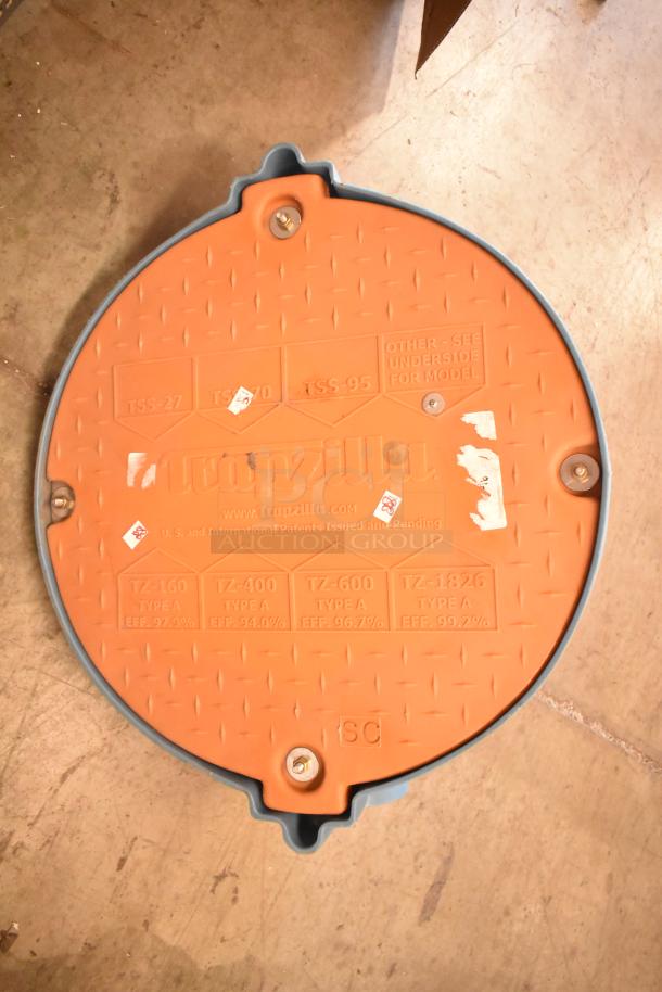 Trapzilla Grease Trap piece, round orange lid with embossed text, patent info, and efficiency ratings, in good condition.