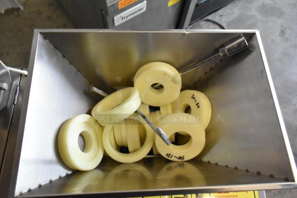 Stainless steel commercial countertop cookie depositor, featuring a metal hopper with several beige dough rings inside.