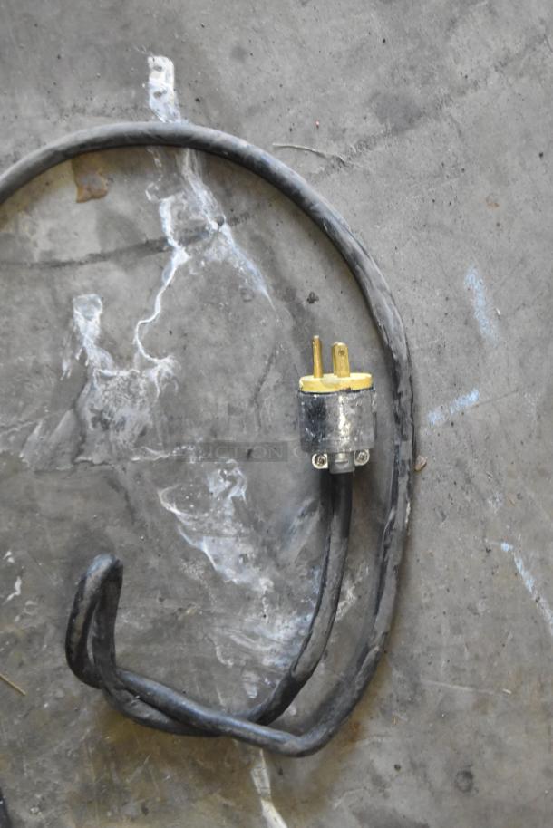 Coiled black power cord with a yellow-tipped plug on concrete surface.