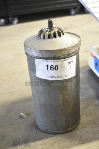 Tall metal container with gear-like top. Visible label reads "160 QTY 1, PCIAuctions.com." Used condition.