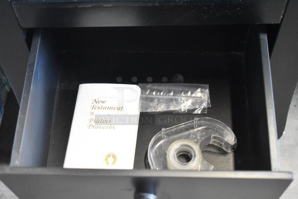 Black wood pattern end table with two drawers, open top drawer showing items including a book and tape, in good condition.