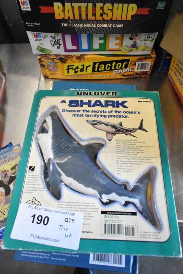 Tier lot including board games like Battleship, Life, and Fear Factor, plus an "Uncover a Shark" educational kit. Auction tag marked "190."