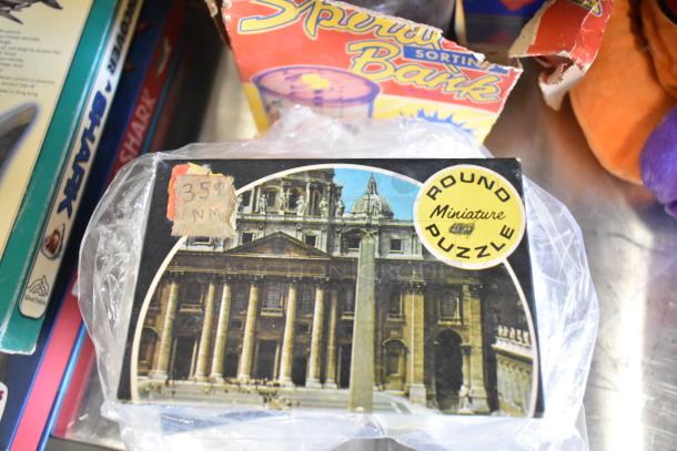 Tier lot featuring board games and books, including a vintage miniature round puzzle with historic building image.