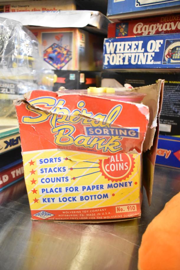 Alt text: Tier lot of various items, including a Spiral Bank sorting toy in damaged packaging, board games, and books.