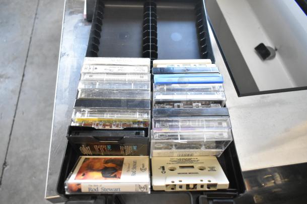 Assorted vintage cassette tapes in black storage case, featuring artists like Rod Stewart and George Michael.