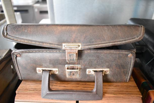 Vintage Marsand leather bag with a worn handle and latch, showcasing signs of wear, resting on a wooden surface.