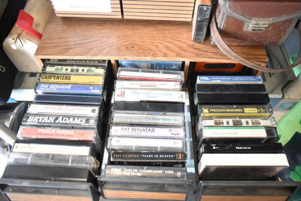 Various vintage cassette tapes and a brown leather Marsand bag. Includes artists like Pat Benatar and Bryan Adams.
