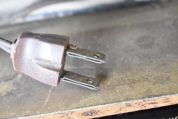 Brown two-prong electrical plug on a worn wooden surface, part of the auction lot including other varied items.