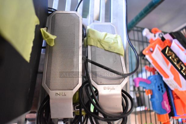 Two Dell speakers with silver mesh fronts, taped for organization. Cables coiled underneath. Part of auction lot.